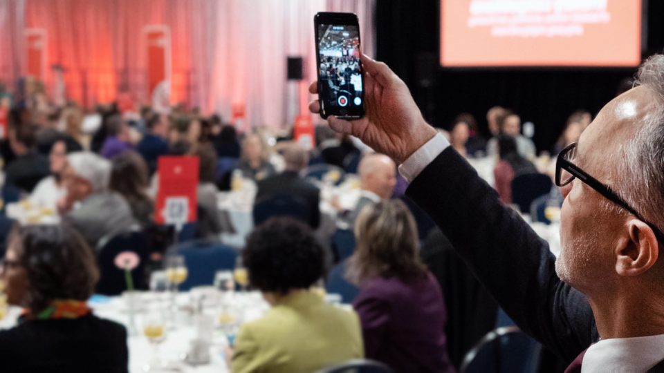 Person taking photo with their cell phone of a busy gala dinner.