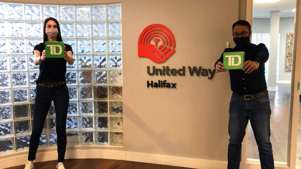 United Way Halifax staff hold green TD boxes in front of the United Way Halifax logo