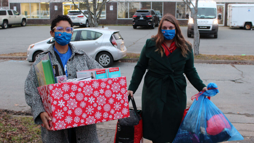 Two volunteers carry boxes and bags with gifts and clothing