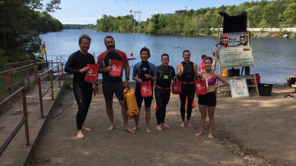 Group of six people wearing wetsuits in front of a lake