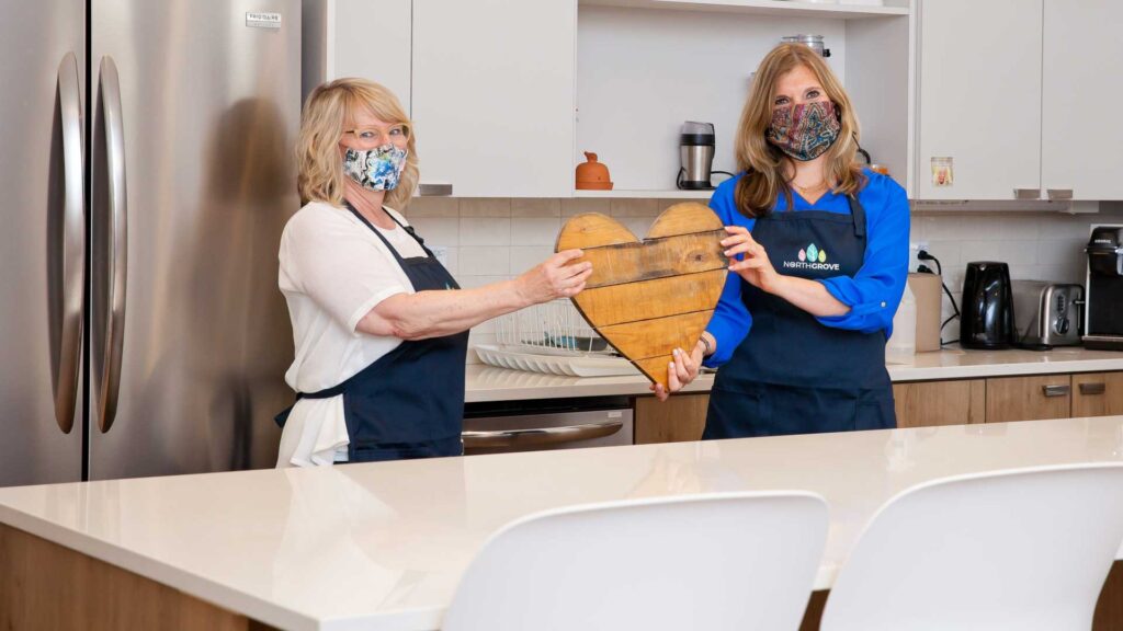 Staff members Sara and Karen in a kitchen holding a wooden heart