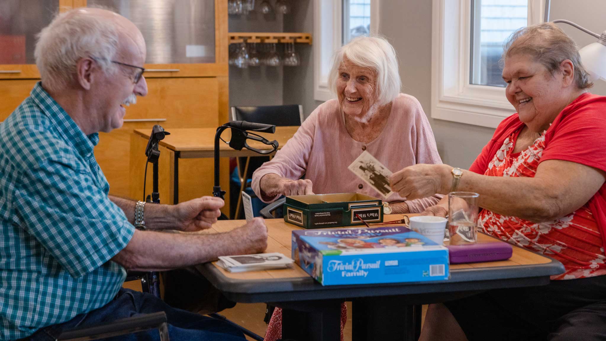3 seniors sitting around a table playing a trivia game and laughing