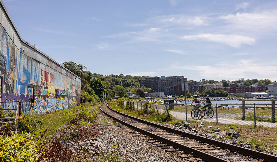 wall covered in graffiti on the left, train tracks in the middle and a bike trail