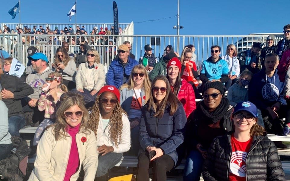 a group of United Way staff sit in the bleachers at a Wanderers soccer game