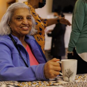 a community member sits at a table at a Beechville Baptist Church even smiling and holding a coffee mug with a tree design on it