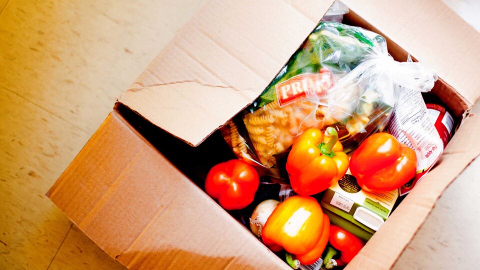 a cardboard box full of food like peppers, tomatoes and pasta
