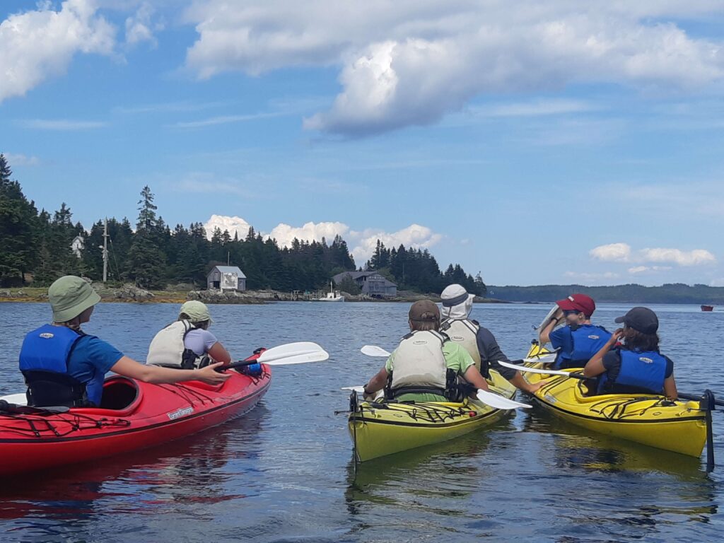 Youth sit in three double kayaks on a bay