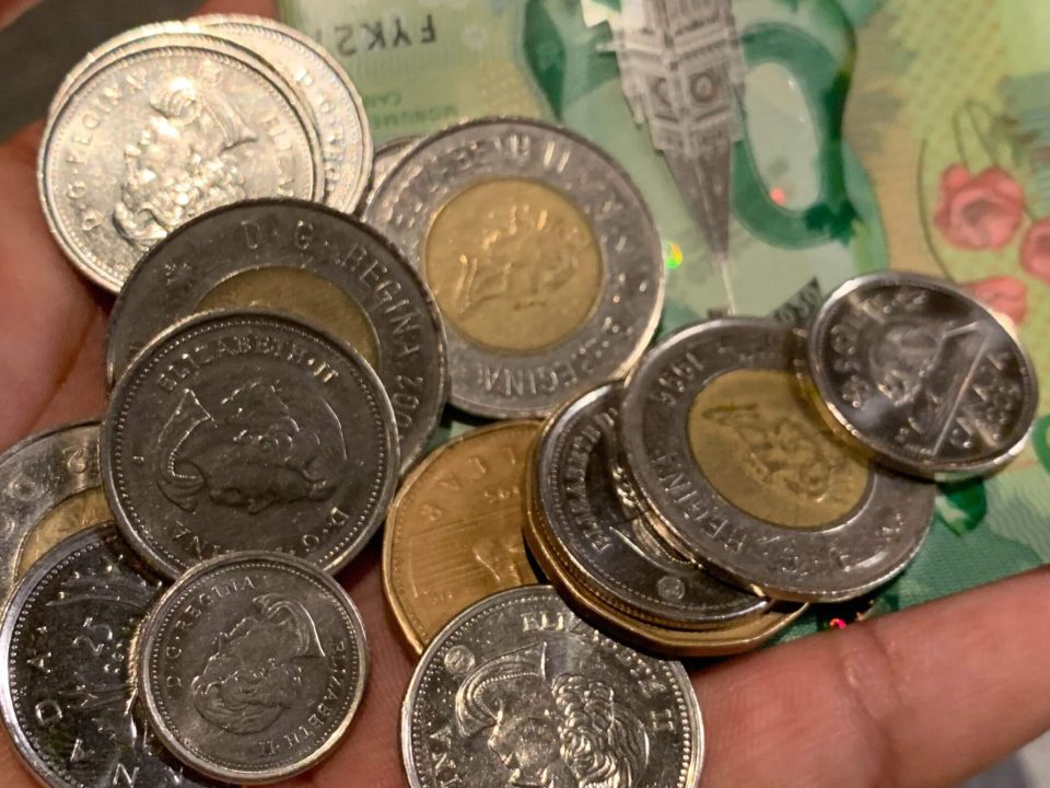 a hand holding coins and a $20 bill - the affordability crisis