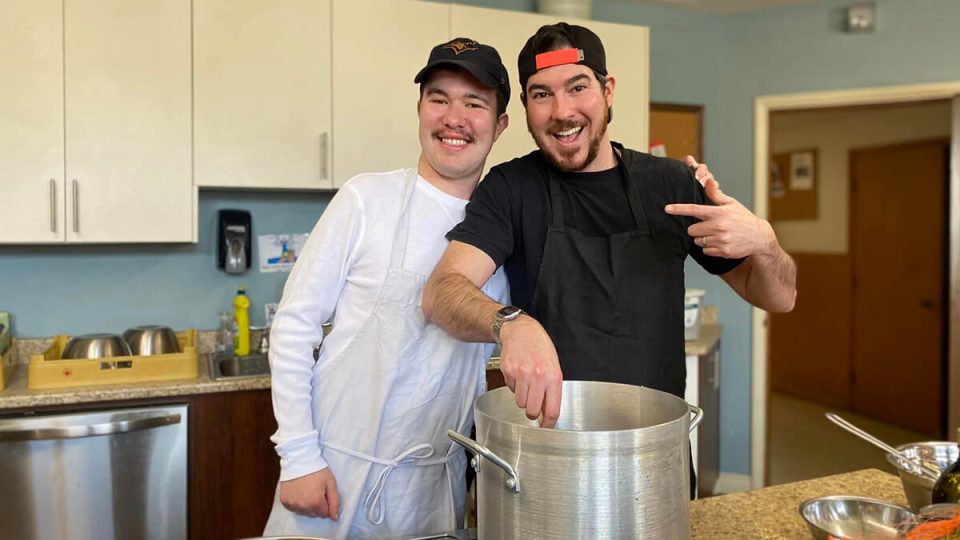 Two people in a kitchen with a big pot on the counter