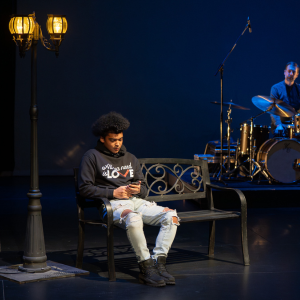 Dylan Young, Youth Ambassador at LOVE Nova Scotia, sitting on stage at Songs of the City 2023 while Aquakultre performs.