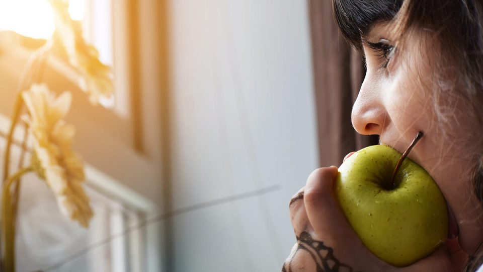 Woman biting into an apple. Being able to meet basic needs like food is essential to addressing poverty
