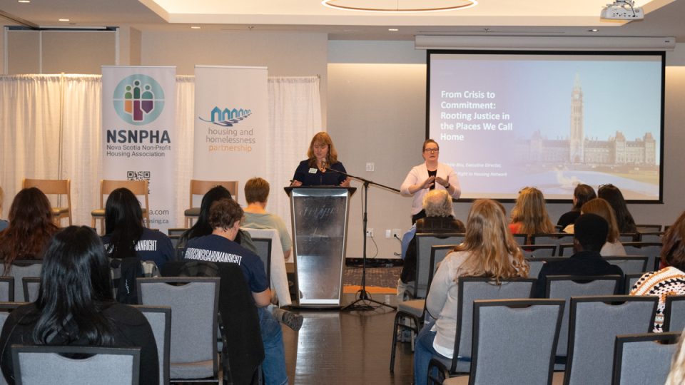 A woman presenting to a crowd at a housing symposium