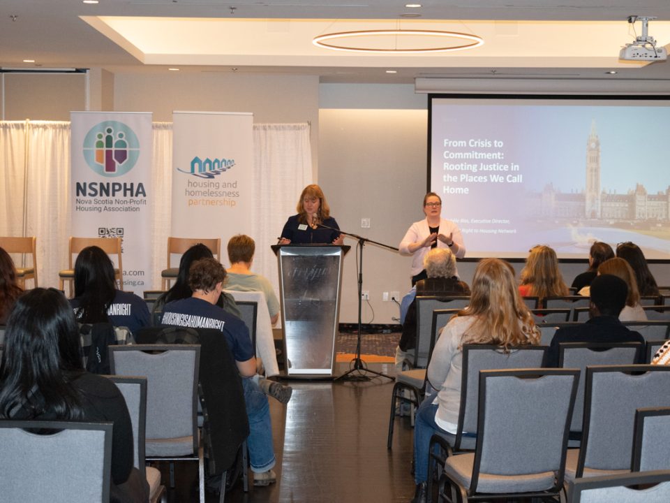 A woman presenting to a crowd at a housing symposium